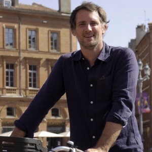 Homme souriant devant Restaurant Emile Toulouse, avec un vélo.